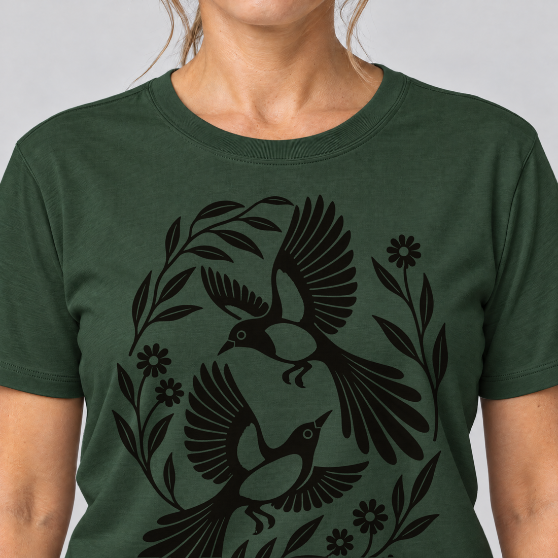 Nahaufnahme des Drucks: Elsternpaar im Scherenschnitt – T-Shirt Unisex in Flaschengrün, von einer Frau getragen