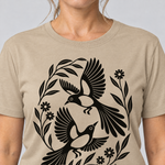 Nahaufnahme des Drucks: Elsternpaar im Scherenschnitt – T-Shirt Unisex in Sand, von einer Frau getragen