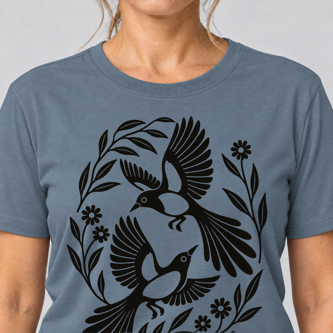 Nahaufnahme des Drucks: Elsternpaar im Scherenschnitt – T-Shirt Unisex in Steinblau, von einer Frau getragen