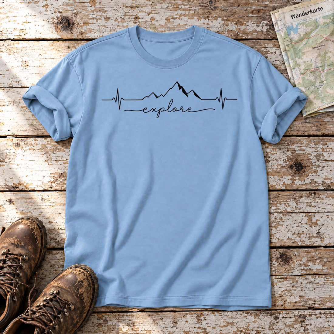 Explore Herzschlag – T-Shirt Unisex in Himmelblau, flach liegend auf alten Holzbrettern mit Wanderschuhen und Wanderkarte.