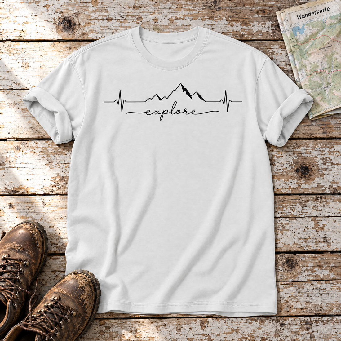 Explore Herzschlag – T-Shirt Unisex in Weiß, flach liegend auf alten Holzbrettern mit Wanderschuhen und Wanderkarte.