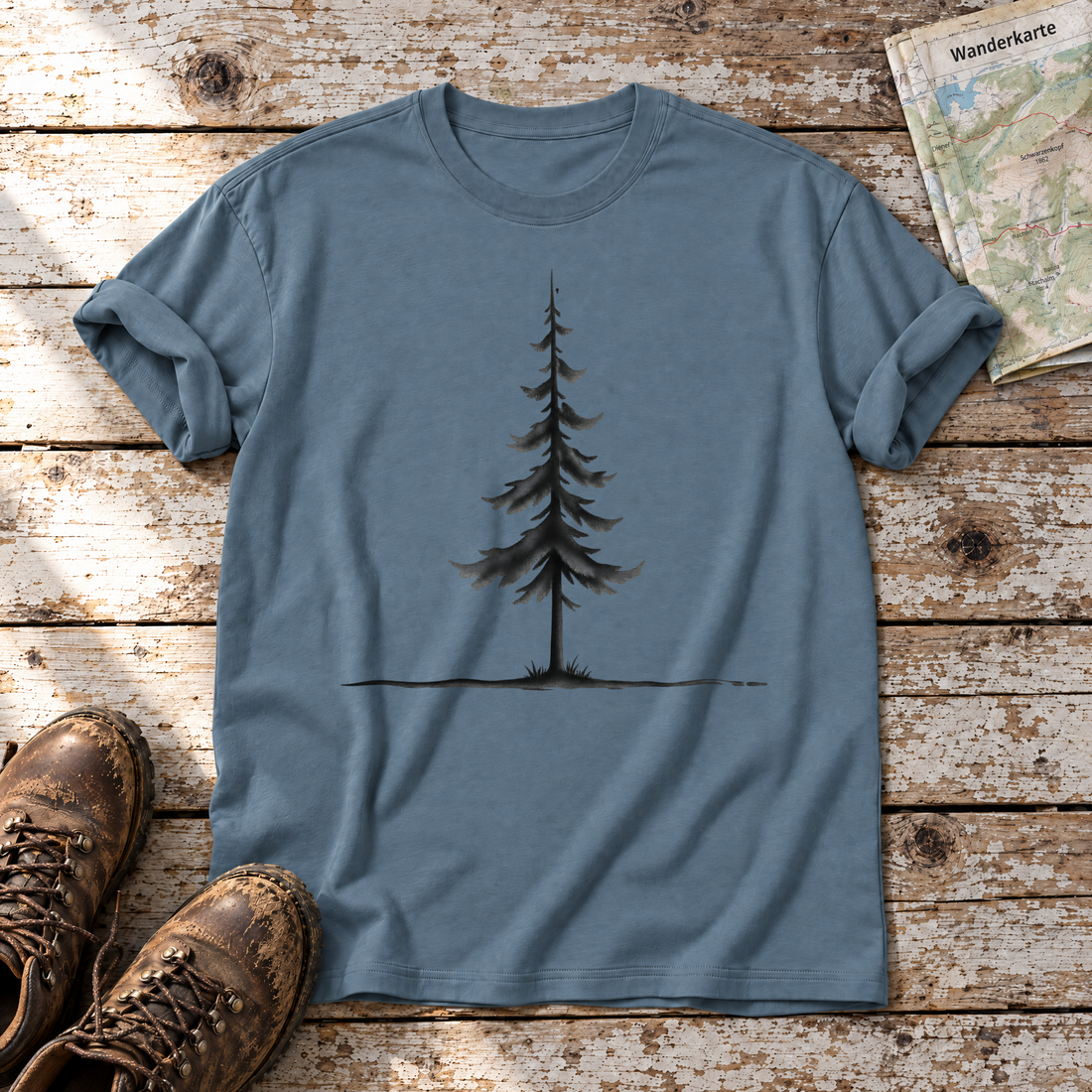 Fichte am Horizont – T-Shirt Unisex in Steinblau, flach liegend auf alten Holzbrettern mit Wanderschuhen und Wanderkarte.