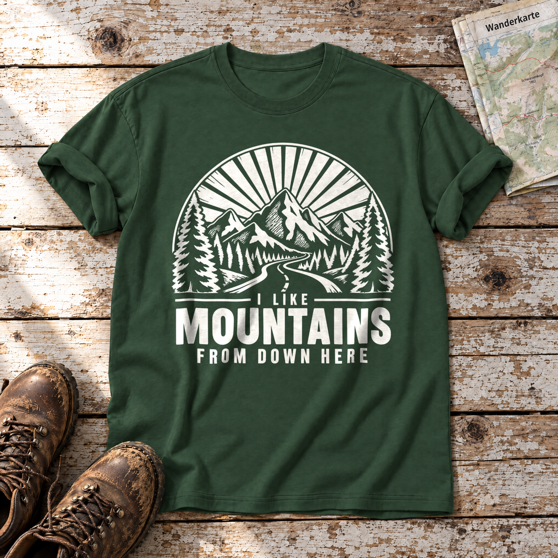 I like mountains from down here – T-Shirt Unisex in Flaschengrün, flach liegend auf alten Holzbrettern mit Wanderschuhen und Wanderkarte.