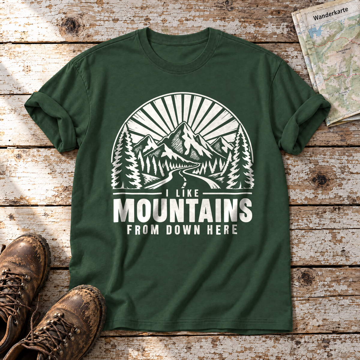 I like mountains from down here – T-Shirt Unisex in Flaschengrün, flach liegend auf alten Holzbrettern mit Wanderschuhen und Wanderkarte.