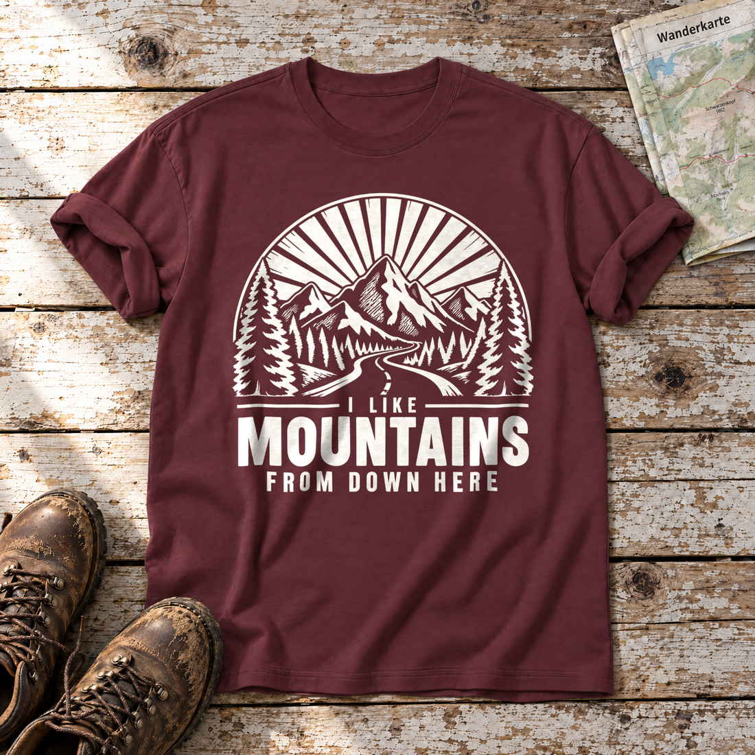 I like mountains from down here – T-Shirt Unisex in Bordeaux, flach liegend auf alten Holzbrettern mit Wanderschuhen und Wanderkarte.