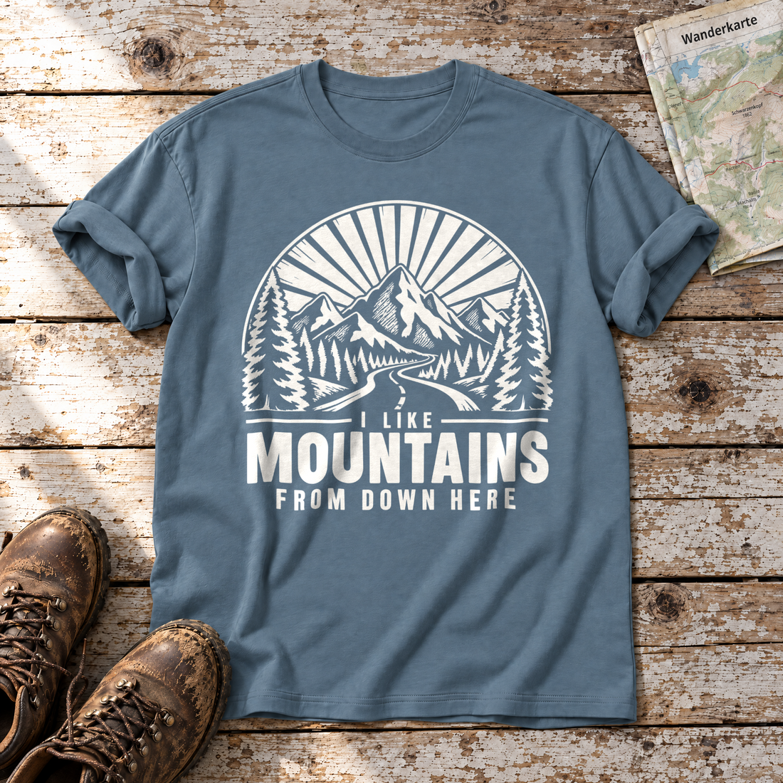 I like mountains from down here – T-Shirt Unisex in Steinblau, flach liegend auf alten Holzbrettern mit Wanderschuhen und Wanderkarte.