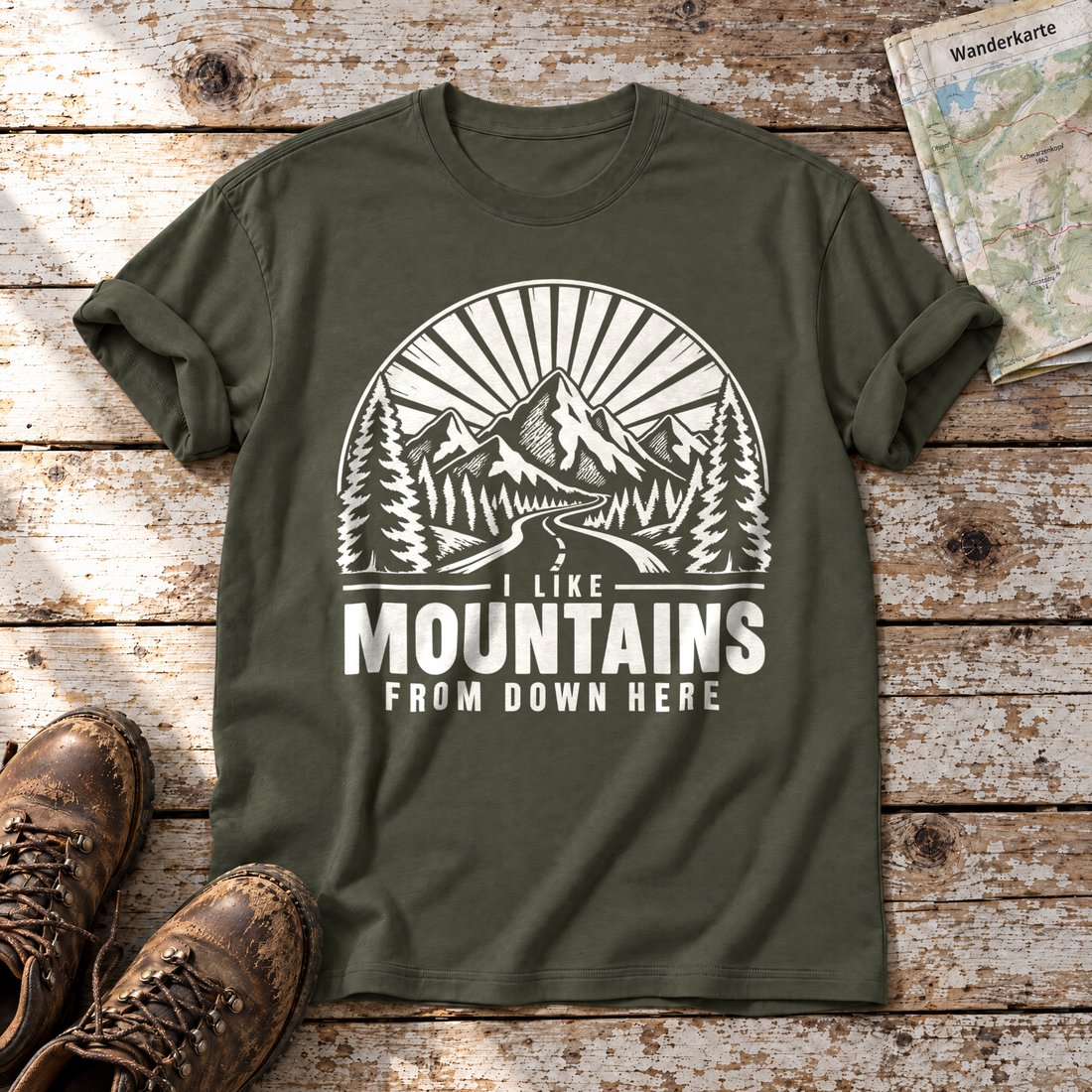I like mountains from down here – T-Shirt Unisex in Oliv, flach liegend auf alten Holzbrettern mit Wanderschuhen und Wanderkarte.