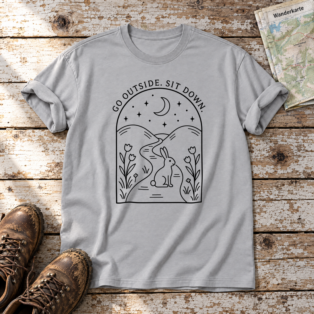 Go outside. Sit down. – T-Shirt Unisex in Hellgrau, flach liegend auf alten Holzbrettern mit Wanderschuhen und Wanderkarte.