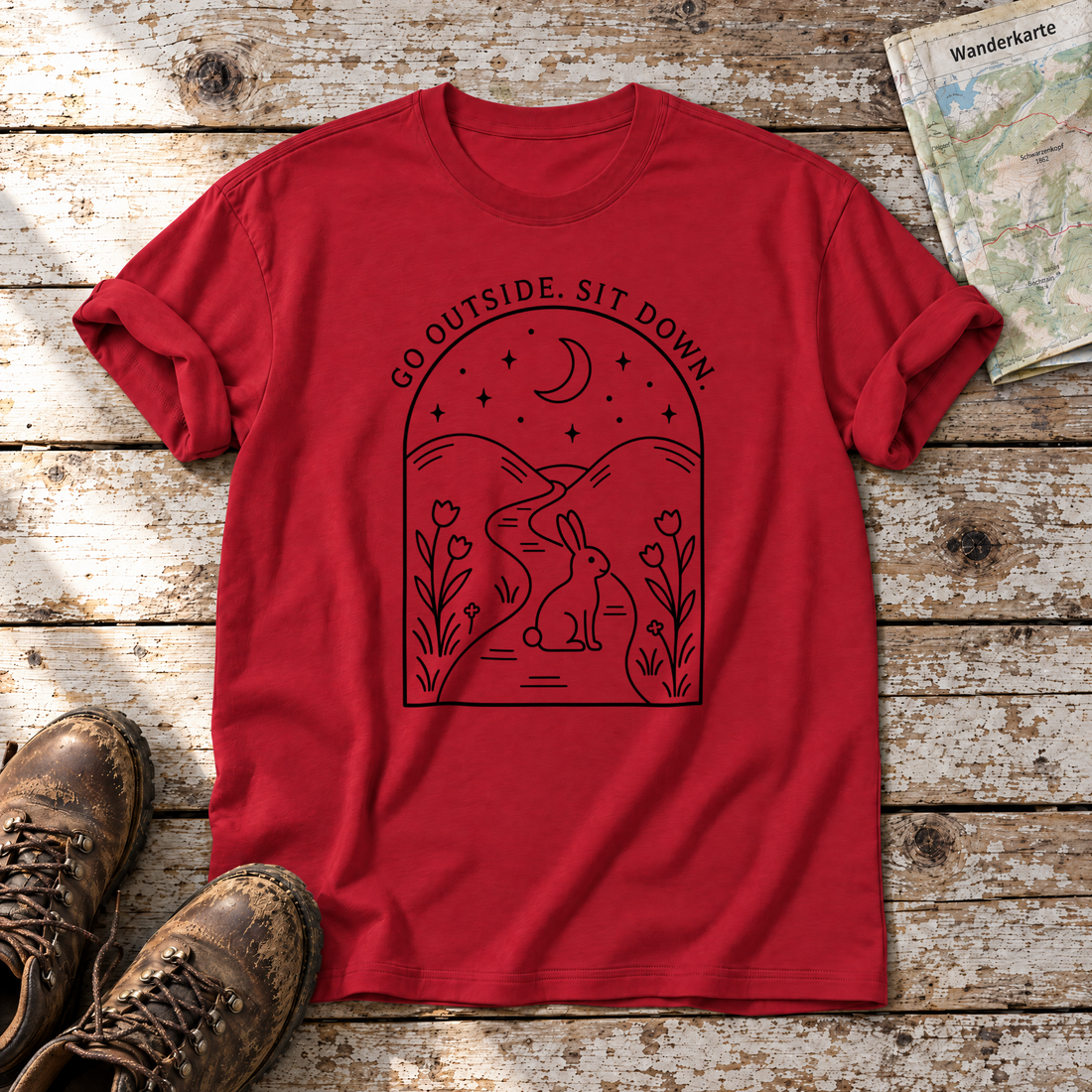 Go outside. Sit down. – T-Shirt Unisex in Rot, flach liegend auf alten Holzbrettern mit Wanderschuhen und Wanderkarte.
