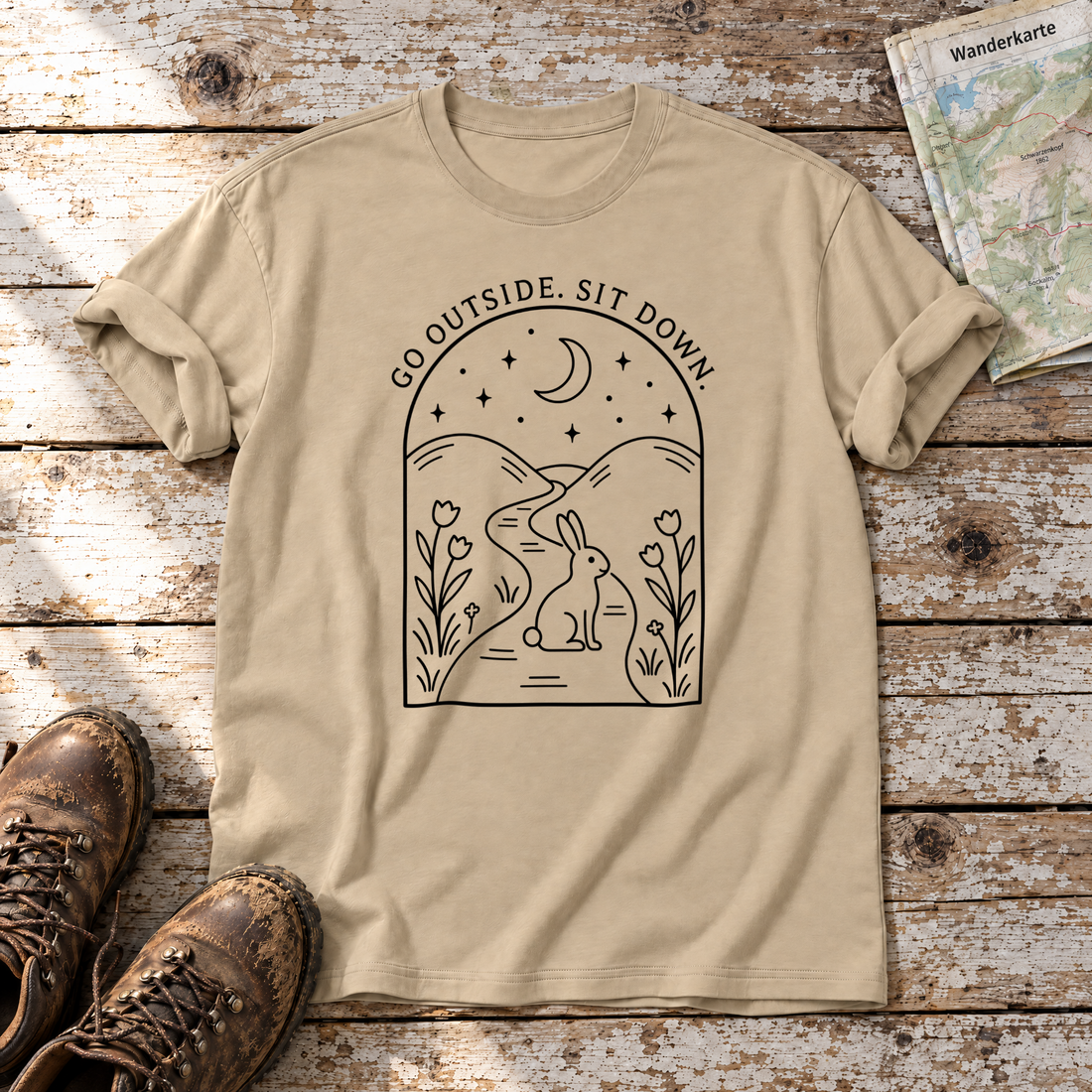 Go outside. Sit down. – T-Shirt Unisex in Sand, flach liegend auf alten Holzbrettern mit Wanderschuhen und Wanderkarte.