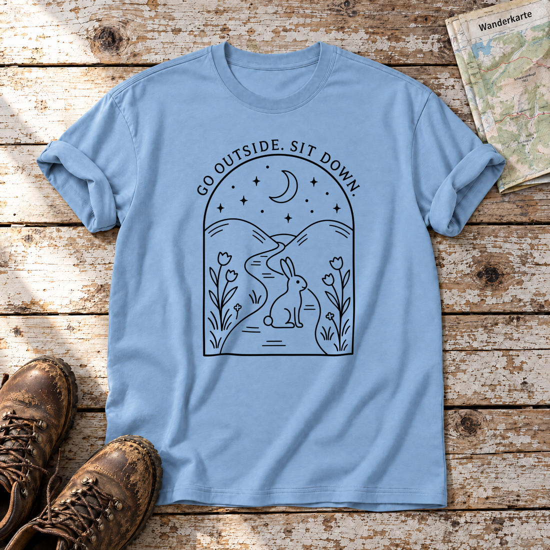Go outside. Sit down. – T-Shirt Unisex in Himmelblau, flach liegend auf alten Holzbrettern mit Wanderschuhen und Wanderkarte.