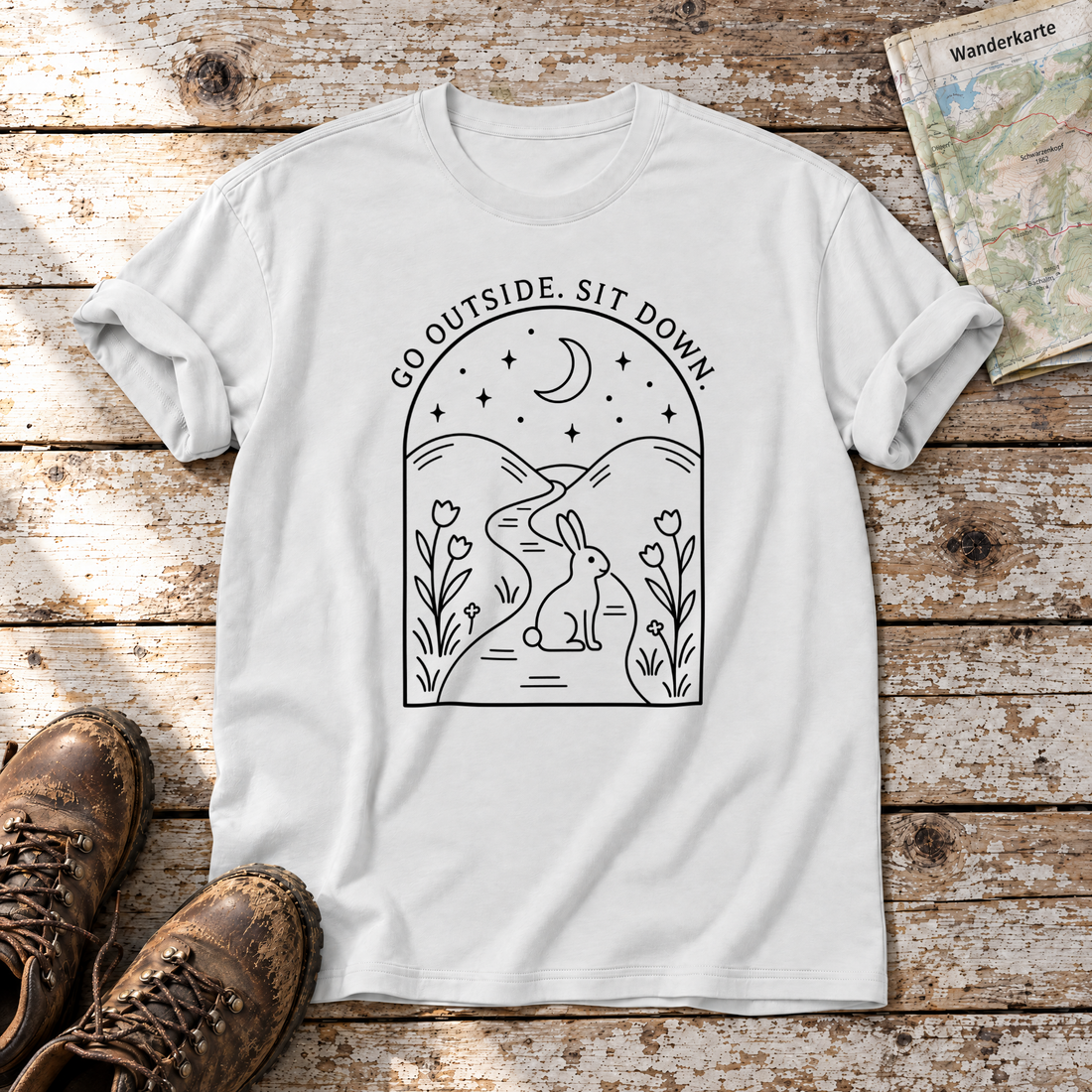 Go outside. Sit down. – T-Shirt Unisex in Weiß, flach liegend auf alten Holzbrettern mit Wanderschuhen und Wanderkarte.
