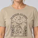 Nahaufnahme des Drucks: Go outside. Sit down. – T-Shirt Unisex in Sand, von einer Frau getragen