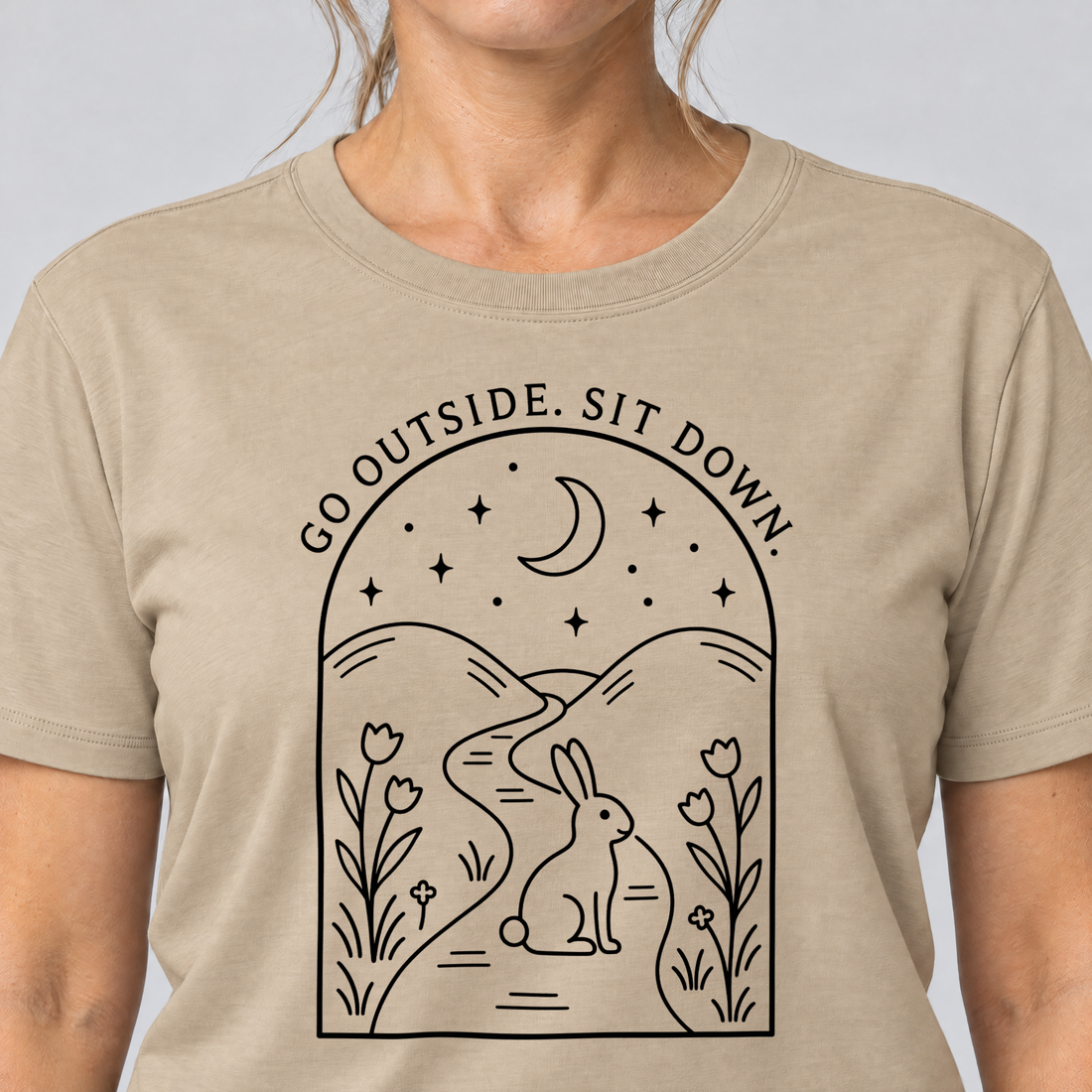 Nahaufnahme des Drucks: Go outside. Sit down. – T-Shirt Unisex in Sand, von einer Frau getragen