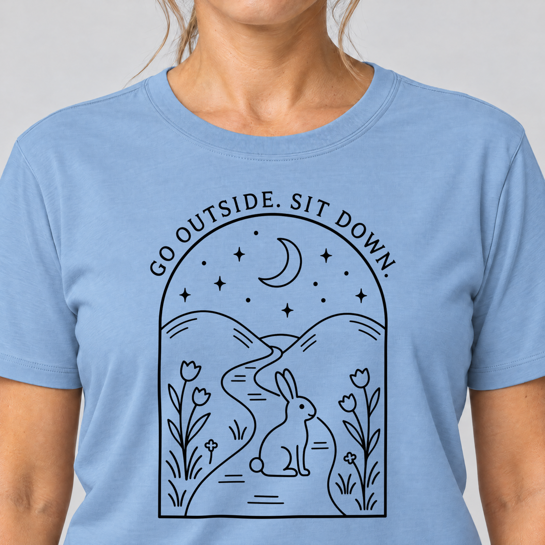 Nahaufnahme des Drucks: Go outside. Sit down. – T-Shirt Unisex in Himmelblau, von einer Frau getragen
