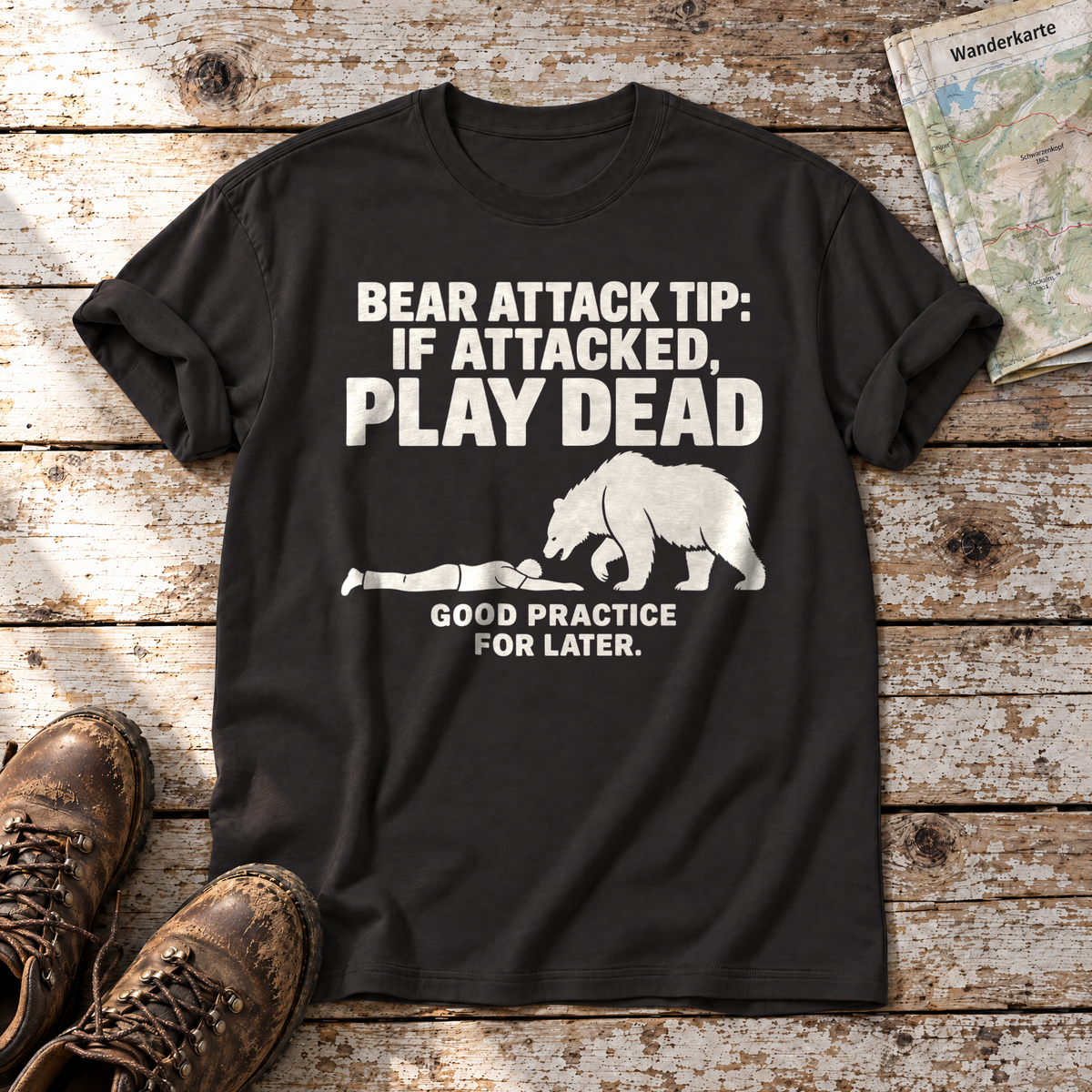 Good Practice for Later – T-Shirt Unisex in Schwarz, flach liegend auf alten Holzbrettern mit Wanderschuhen und Wanderkarte.