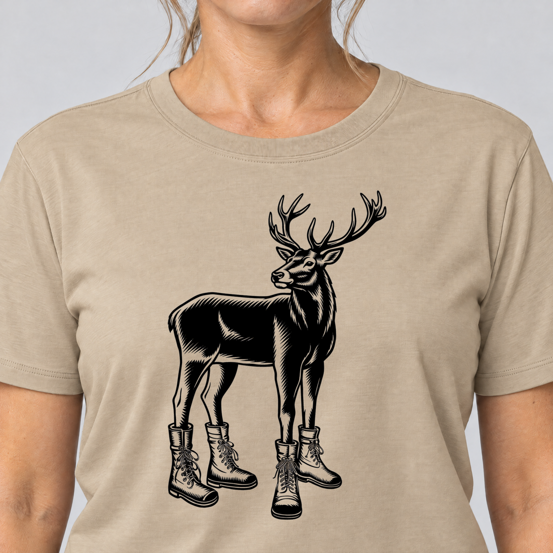 Nahaufnahme des Drucks: Hirsch in Bergschuhen – T-Shirt Unisex in Sand, von einer Frau getragen