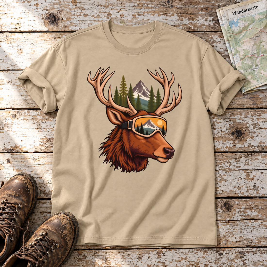 Hirsch mit Skibrille – T-Shirt Unisex in Sand, flach liegend auf alten Holzbrettern mit Wanderschuhen und Wanderkarte.
