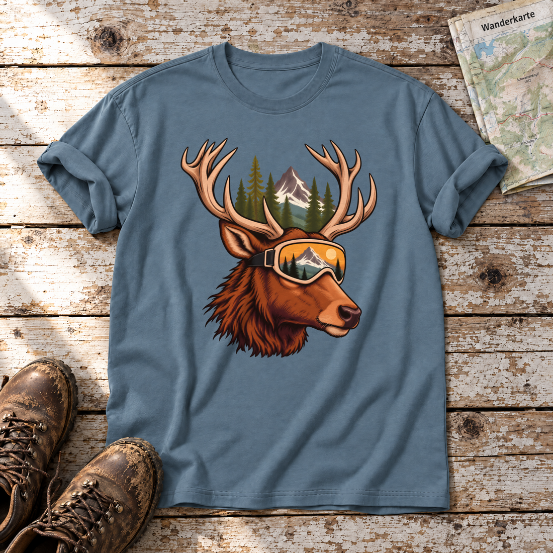 Hirsch mit Skibrille – T-Shirt Unisex in Steinblau, flach liegend auf alten Holzbrettern mit Wanderschuhen und Wanderkarte.