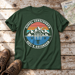 Gipfel verschoben, Hütte gefunden – T-Shirt Unisex in Flaschengrün, flach liegend auf alten Holzbrettern mit Wanderschuhen und Wanderkarte.