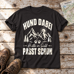Hütte in Sicht, passt schon – T-Shirt Unisex in Schwarz, flach liegend auf alten Holzbrettern mit Wanderschuhen und Wanderkarte.
