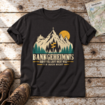 Bankgeheimnis – T-Shirt Unisex in Schwarz, flach liegend auf alten Holzbrettern mit Wanderschuhen und Wanderkarte.