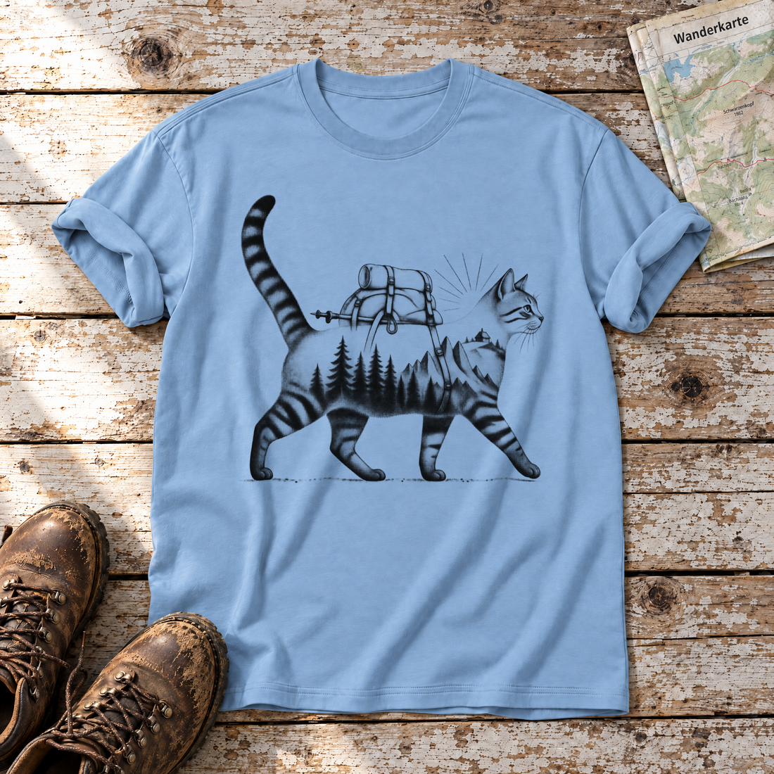 Katze mit Rucksack – T-Shirt Unisex in Himmelblau, flach liegend auf alten Holzbrettern mit Wanderschuhen und Wanderkarte.