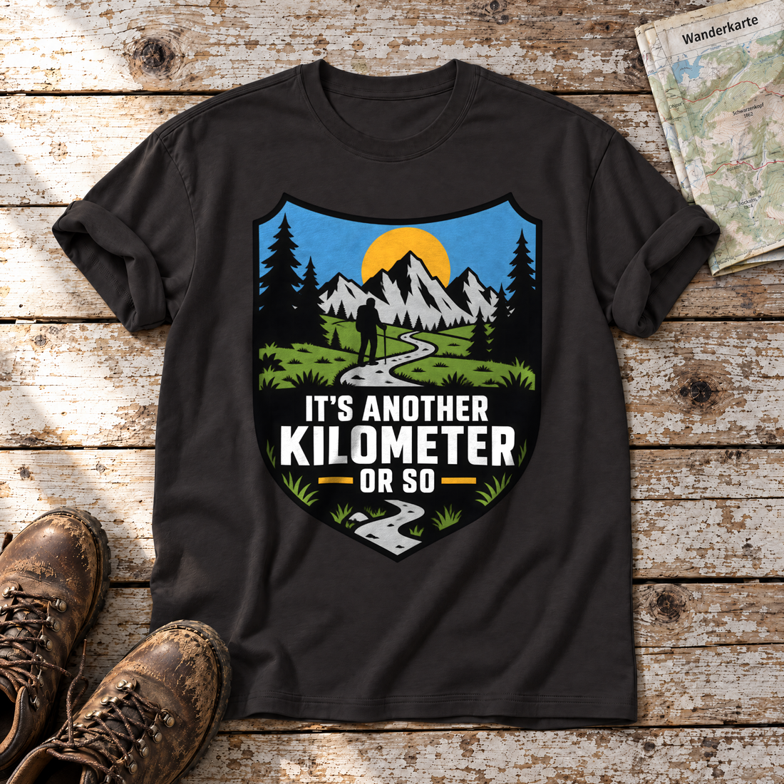 Another Kilometer or So – T-Shirt Unisex in Schwarz, flach liegend auf alten Holzbrettern mit Wanderschuhen und Wanderkarte.