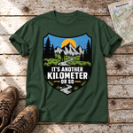 Another Kilometer or So – T-Shirt Unisex in Flaschengrün, flach liegend auf alten Holzbrettern mit Wanderschuhen und Wanderkarte.