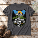 Another Kilometer or So – T-Shirt Unisex in Dunkelgrau, flach liegend auf alten Holzbrettern mit Wanderschuhen und Wanderkarte.