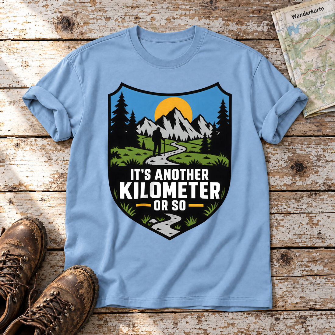 Another Kilometer or So – T-Shirt Unisex in Himmelblau, flach liegend auf alten Holzbrettern mit Wanderschuhen und Wanderkarte.