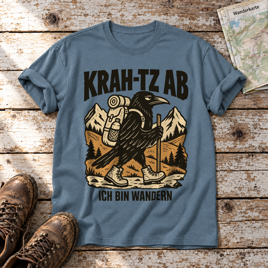 Krah-tz ab – T-Shirt Unisex in Steinblau, flach liegend auf alten Holzbrettern mit Wanderschuhen und Wanderkarte.
