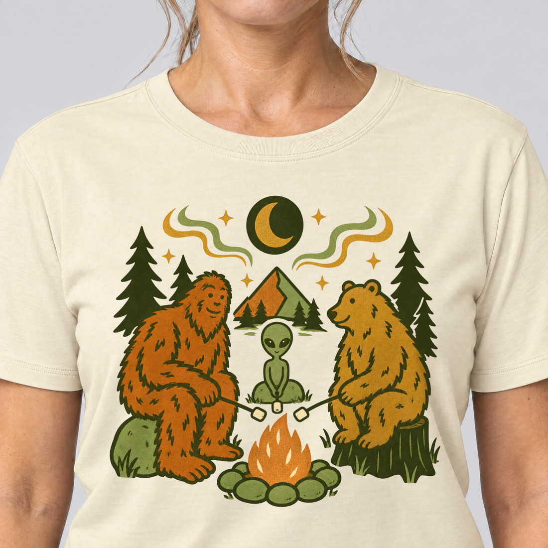 Nahaufnahme des Drucks: Bigfoot, Alien und Bär am Lagerfeuer – T-Shirt Unisex in Natur, von einer Frau getragen