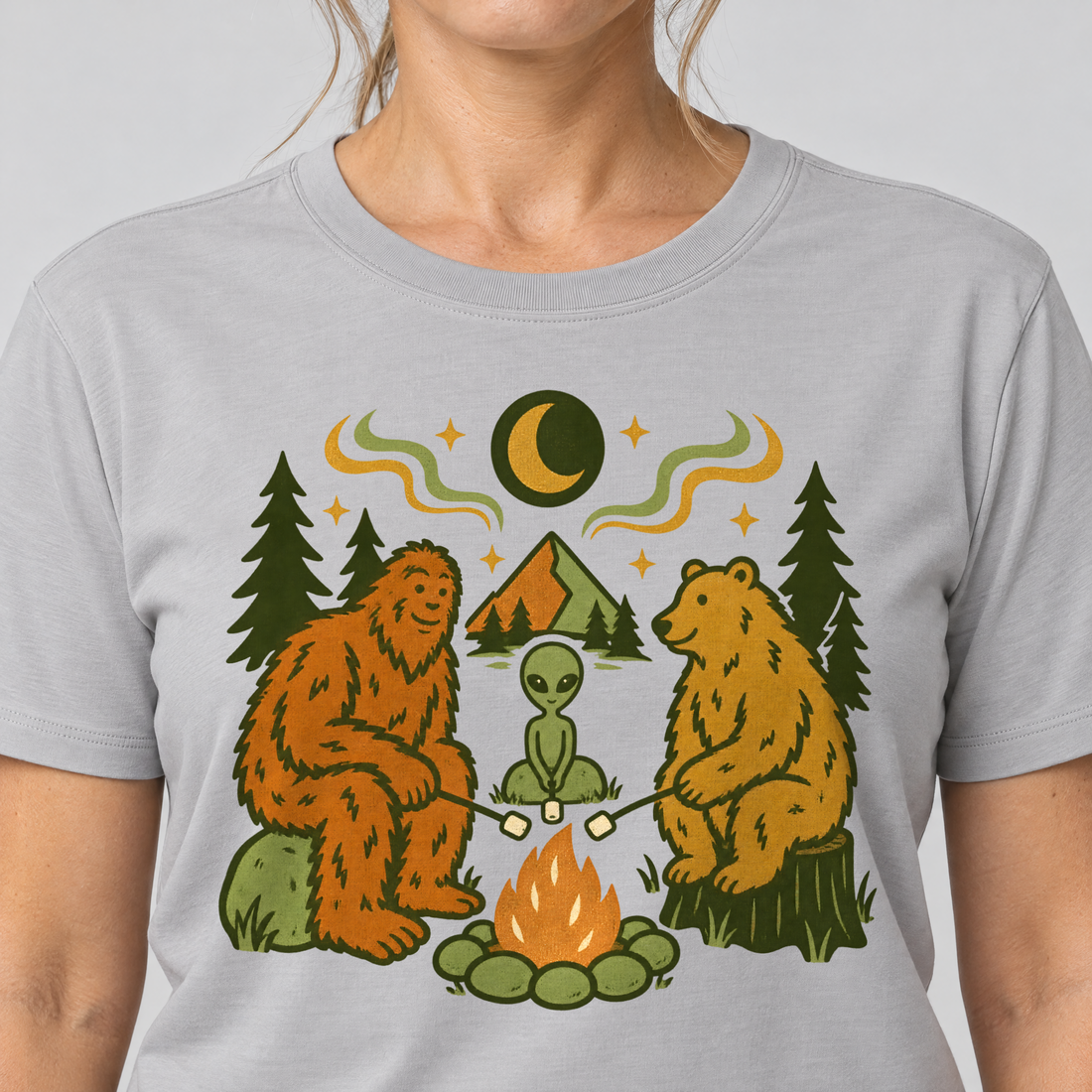 Nahaufnahme des Drucks: Bigfoot, Alien und Bär am Lagerfeuer – T-Shirt Unisex in Hellgrau, von einer Frau getragen