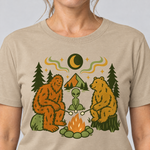 Nahaufnahme des Drucks: Bigfoot, Alien und Bär am Lagerfeuer – T-Shirt Unisex in Sand, von einer Frau getragen
