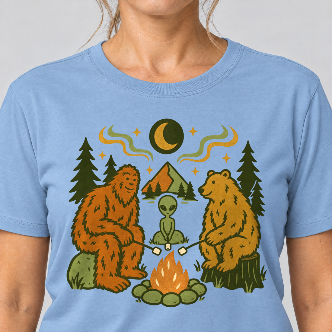 Nahaufnahme des Drucks: Bigfoot, Alien und Bär am Lagerfeuer – T-Shirt Unisex in Himmelblau, von einer Frau getragen
