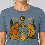 Nahaufnahme des Drucks: Bigfoot, Alien und Bär am Lagerfeuer – T-Shirt Unisex in Steinblau, von einer Frau getragen
