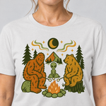 Nahaufnahme des Drucks: Bigfoot, Alien und Bär am Lagerfeuer – T-Shirt Unisex in Weiß, von einer Frau getragen