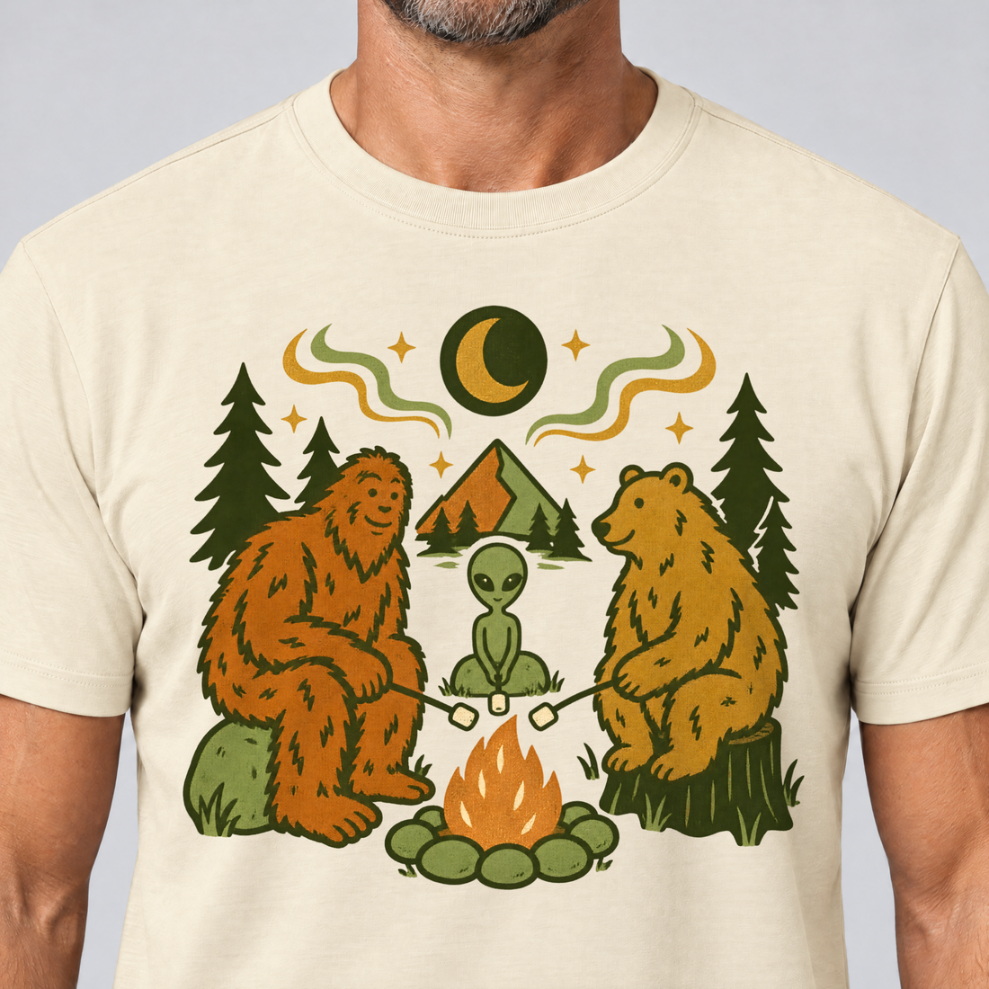 Nahaufnahme des Drucks: Bigfoot, Alien und Bär am Lagerfeuer – T-Shirt Unisex in Natur, von einem Mann getragen