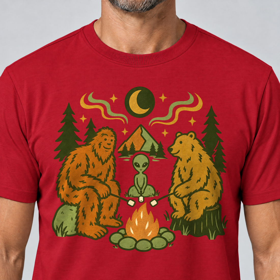 Nahaufnahme des Drucks: Bigfoot, Alien und Bär am Lagerfeuer – T-Shirt Unisex in Rot, von einem Mann getragen
