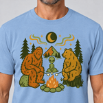 Nahaufnahme des Drucks: Bigfoot, Alien und Bär am Lagerfeuer – T-Shirt Unisex in Himmelblau, von einem Mann getragen