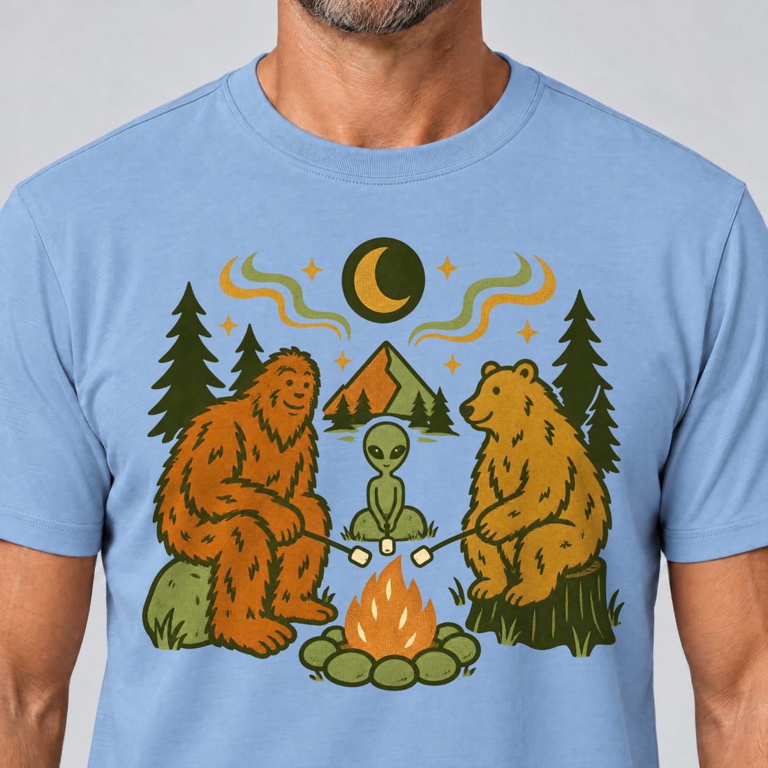 Nahaufnahme des Drucks: Bigfoot, Alien und Bär am Lagerfeuer – T-Shirt Unisex in Himmelblau, von einem Mann getragen