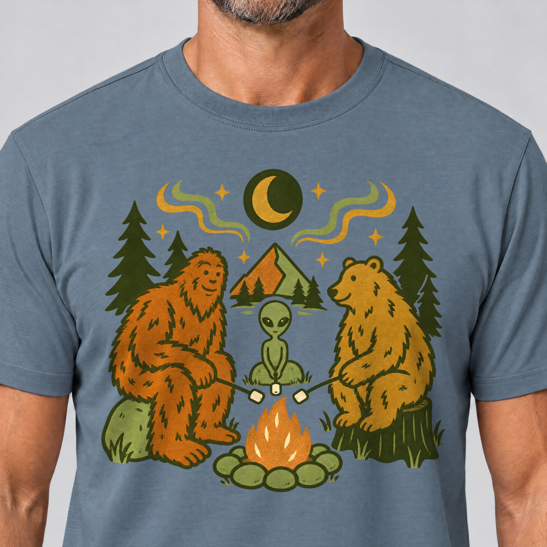 Nahaufnahme des Drucks: Bigfoot, Alien und Bär am Lagerfeuer – T-Shirt Unisex in Steinblau, von einem Mann getragen