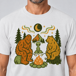 Nahaufnahme des Drucks: Bigfoot, Alien und Bär am Lagerfeuer – T-Shirt Unisex in Weiß, von einem Mann getragen