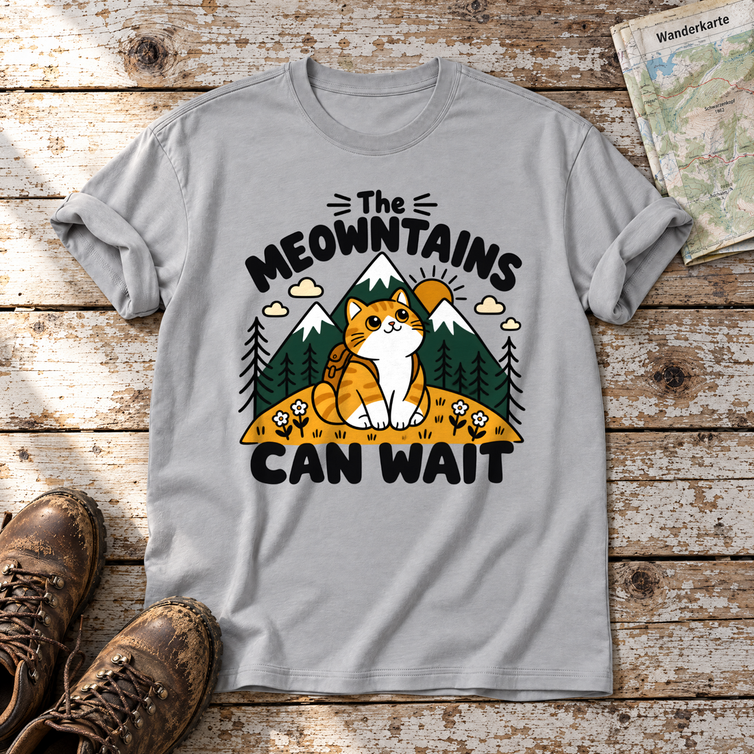 The Meowntains can wait – T-Shirt Unisex in Hellgrau, flach liegend auf alten Holzbrettern mit Wanderschuhen und Wanderkarte.