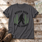 Never seen at the summit – T-Shirt Unisex in Dunkelgrau, flach liegend auf alten Holzbrettern mit Wanderschuhen und Wanderkarte.