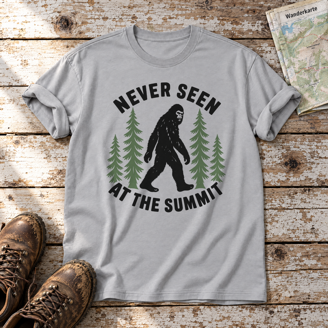 Never seen at the summit – T-Shirt Unisex in Hellgrau, flach liegend auf alten Holzbrettern mit Wanderschuhen und Wanderkarte.