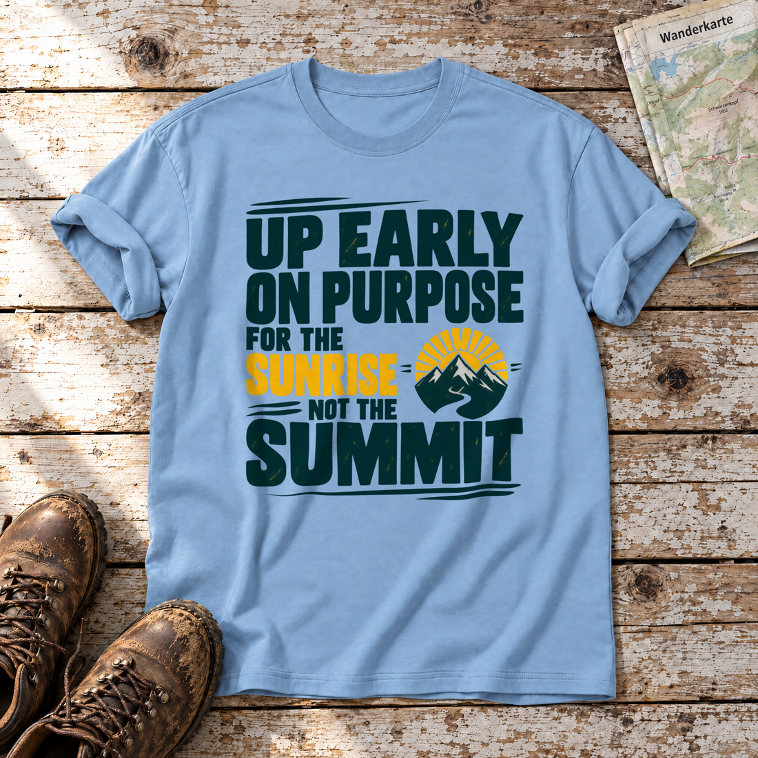 For the Sunrise, Not the Summit – T-Shirt Unisex in Himmelblau, flach liegend auf alten Holzbrettern mit Wanderschuhen und Wanderkarte.