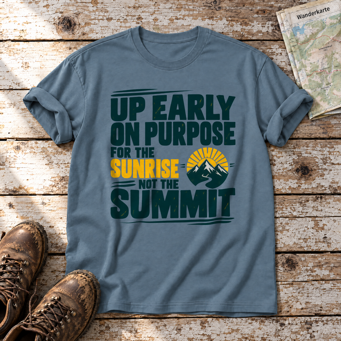 For the Sunrise, Not the Summit – T-Shirt Unisex in Steinblau, flach liegend auf alten Holzbrettern mit Wanderschuhen und Wanderkarte.