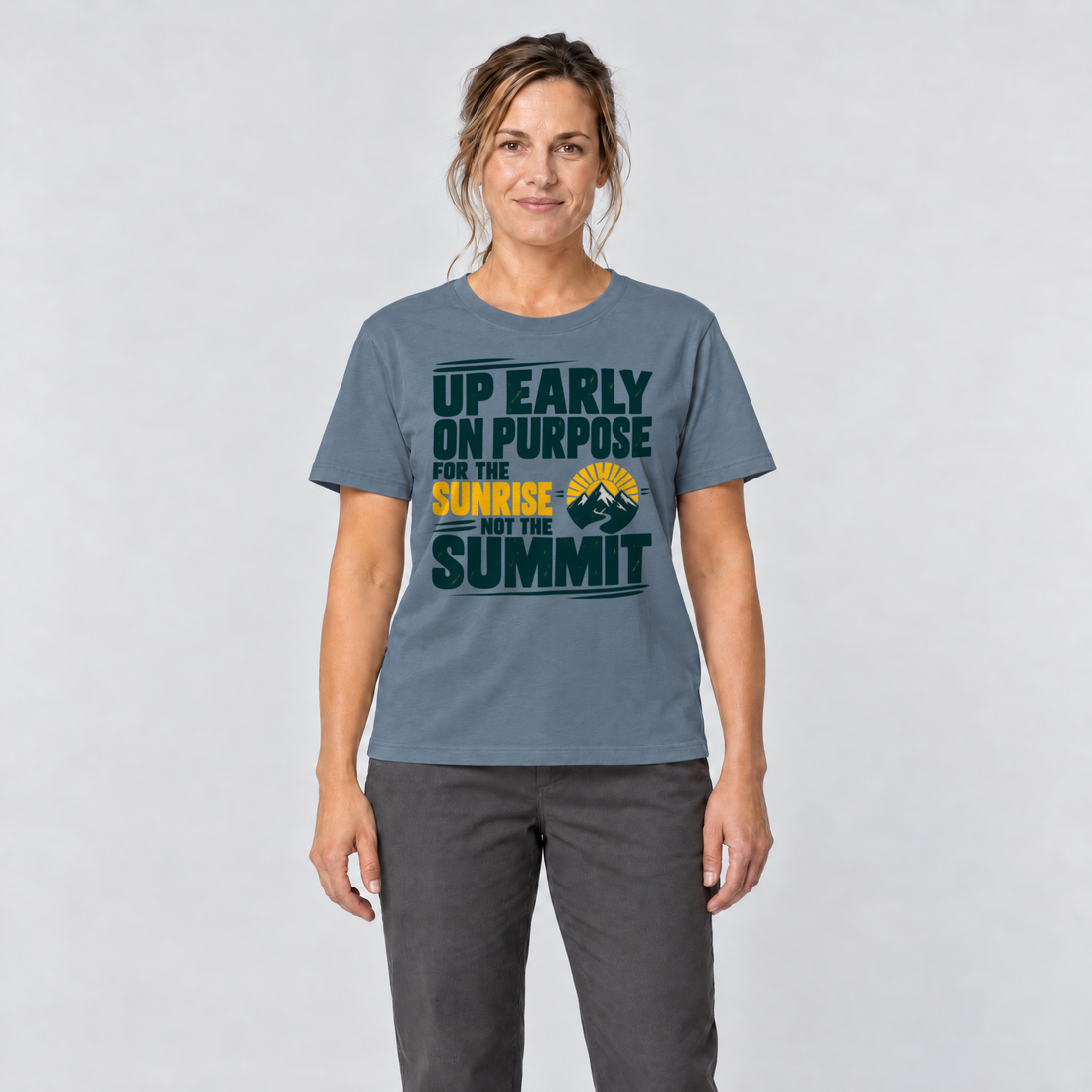 Frau trägt For the Sunrise, Not the Summit – T-Shirt Unisex in Steinblau, Ansicht von vorn